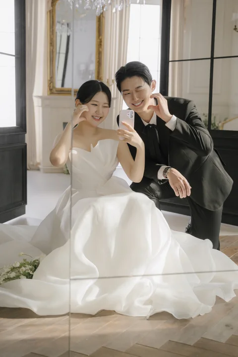 거울 앞에서 손으로 하트를 만들며 함께 사진을 찍는 두 사람